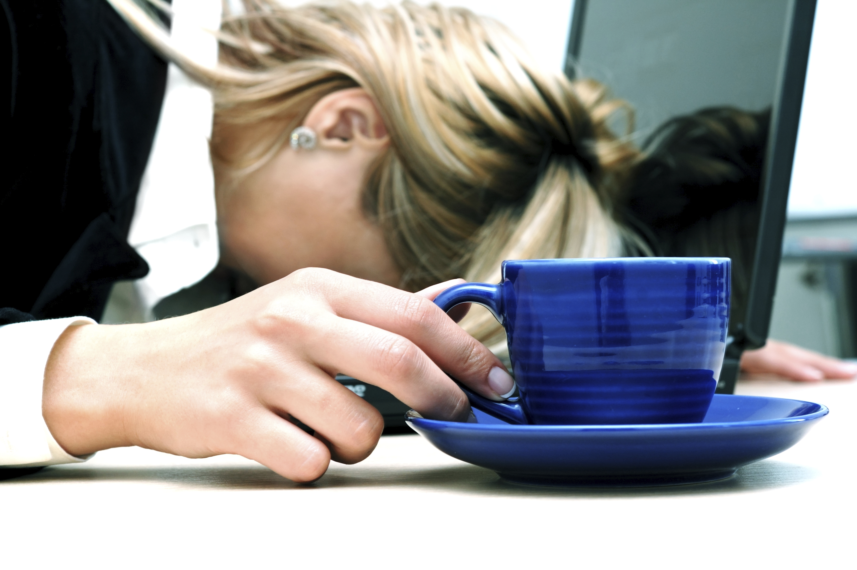 Tired woman are sleeping and holding cup. Laptop is situated on the table.